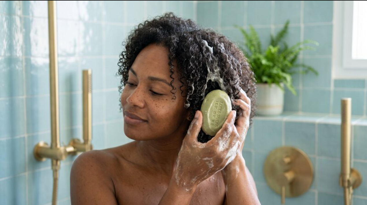 femme aux cheveux boucles se lave les cheveux avec un shampoing solide vert