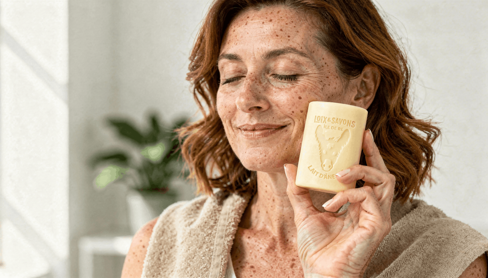 Femme tenant un savon artisanal au lait d'ânesse rectangulaire couleur ivoire près du visage